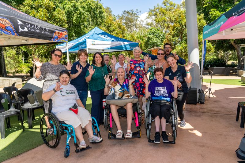 A photo of a group of people in a park, smiling and waving at the camera.